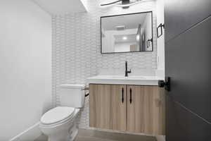 Half bath in basement with vanity light,tile floors, and decorative backsplash.