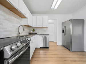 Kitchen with stainless steel appliances, light stone counters, white cabinetry, tasteful backsplash, and light wood-type flooring
