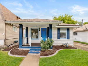 View of front of property featuring covered porch, a shingled roof, and a front yard