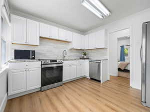 Kitchen featuring appliances with stainless steel finishes, backsplash, white cabinetry, light wood finished floors, and crown molding