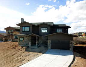 View of front of property featuring stone siding, an attached garage, concrete driveway, and a chimney