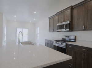 Kitchen with appliances with stainless steel finishes, light stone countertops, a center island with sink, recessed lighting, and dark brown cabinetry