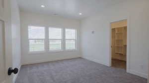 Unfurnished bedroom with light carpet, a spacious closet, and recessed lighting