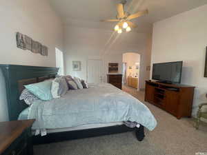 Bedroom with light colored carpet, ceiling fan, arched walkways, high vaulted ceiling, and ensuite bathroom