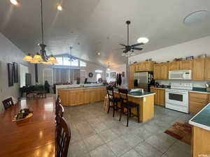 Kitchen featuring white appliances, a kitchen bar, pendant lighting, dark tile patterned floors, and high vaulted ceiling