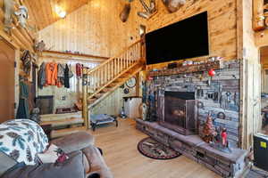 Living area with wood walls, wood finished floors, a fireplace, high vaulted ceiling, and stairs