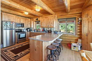 Kitchen featuring appliances with stainless steel finishes, light wood finished floors, healthy amount of natural light, a kitchen breakfast bar, and rustic walls