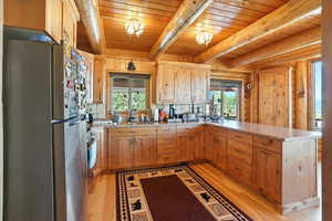 Kitchen with appliances with stainless steel finishes, light countertops, healthy amount of natural light, light wood-type flooring, and a wood ceiling with exposed beams