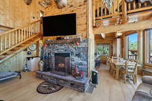 Living area featuring a stone fireplace, wood walls, wood finished floors, stairway, and a high ceiling