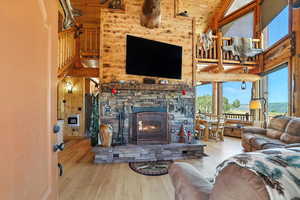 Living area featuring plenty of natural light, high vaulted ceiling, wood finished floors, wood walls, and a stone fireplace