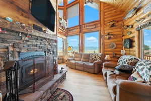 Living area with wood finished floors, high vaulted ceiling, a stone fireplace, wooden ceiling, and rustic walls