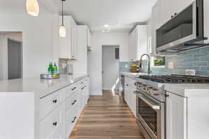 Kitchen featuring stainless steel appliances, white cabinets, light stone countertops, pendant lighting, and light wood finished floors