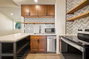 Kitchen with open shelves, appliances with stainless steel finishes, brown cabinetry, light countertops, and recessed lighting