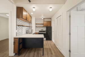 Kitchen featuring backsplash, light countertops, open shelves, stainless steel appliances, and brown cabinetry