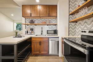 Kitchen with open shelves, appliances with stainless steel finishes, brown cabinetry, light countertops, and decorative backsplash
