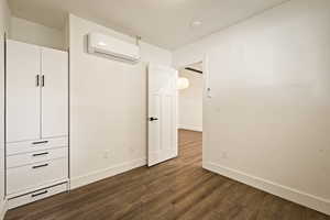 Unfurnished bedroom featuring dark wood-type flooring and a wall unit AC