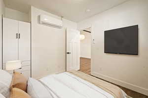 Bedroom with a wall mounted air conditioner and wood finished floors