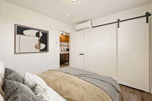 Bedroom featuring a barn door, wood finished floors, and a wall mounted AC