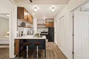 Kitchen featuring backsplash, open shelves, a breakfast bar area, appliances with stainless steel finishes, and brown cabinetry