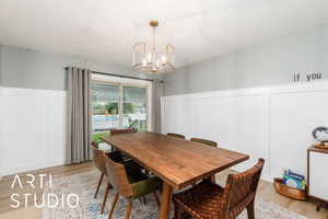 Dining room featuring a decorative wall, wainscoting, light wood-style floors, and a chandelier