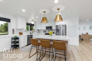 Kitchen featuring appliances with stainless steel finishes, white cabinetry, decorative light fixtures, light stone counters, and recessed lighting