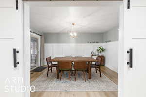 Dining space featuring a barn door, a decorative wall, a wainscoted wall, light wood-style flooring, and a chandelier