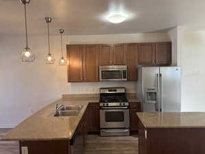 Kitchen with stainless steel appliances, dark wood-type flooring, hanging light fixtures, a peninsula, and a textured ceiling