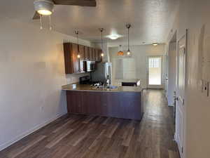 Kitchen featuring a peninsula, a textured ceiling, appliances with stainless steel finishes, dark wood-style flooring, and hanging light fixtures