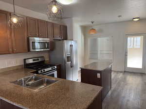Kitchen with stainless steel appliances, pendant lighting, dark countertops, a kitchen island, and dark wood finished floors