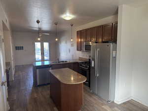 Kitchen featuring stainless steel appliances, decorative light fixtures, a textured ceiling, dark wood-style flooring, and a peninsula