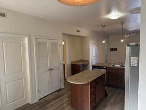 Kitchen with a textured ceiling, appliances with stainless steel finishes, dark wood-style floors, pendant lighting, and dark brown cabinetry