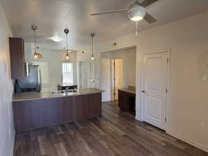 Kitchen featuring a peninsula, dark wood-style floors, hanging light fixtures, a textured ceiling, and a ceiling fan