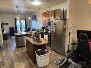 Kitchen with open floor plan, hanging light fixtures, a peninsula, stainless steel appliances, and a textured ceiling
