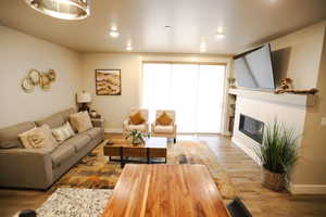 Living room with wood finished floors, a glass covered fireplace, and recessed lighting