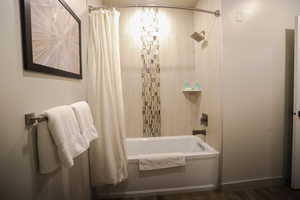 Bathroom with shower / bath combination with curtain and dark wood-style flooring