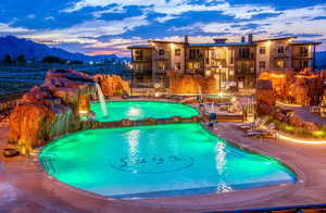 Pool at dusk featuring a patio, a mountain view, a pool with connected hot tub, and a balcony