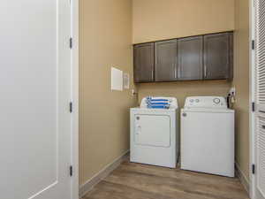 Laundry area featuring wood finished floors, cabinet space, and washing machine and clothes dryer