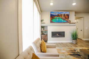 Living room featuring wood finished floors, a glass covered fireplace, and recessed lighting