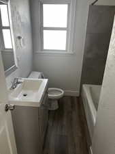 Full bathroom featuring a textured wall, vanity, dark wood-style floors, healthy amount of natural light, and shower / tub combination