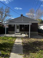 Rear view of property featuring covered porch, a shingled roof, and brick siding