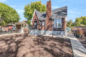 View of front of property featuring a chimney, brick siding, and roof with shingles