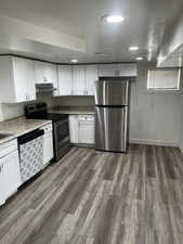 Kitchen with white cabinetry, appliances with stainless steel finishes, recessed lighting, dark wood-style floors, and light stone countertops