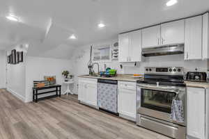 Kitchen featuring appliances with stainless steel finishes, white cabinetry, under cabinet range hood, light wood-style flooring, and recessed lighting