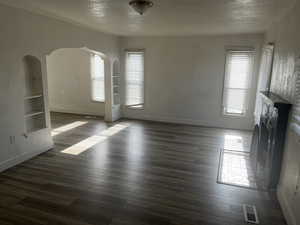 Unfurnished living room featuring built in features, a textured ceiling, dark wood-type flooring, and arched walkways