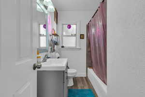 Full bathroom with vanity, shower / bath combination with curtain, dark wood finished floors, and a textured wall
