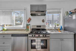 Kitchen featuring stainless steel appliances, under cabinet range hood, and gray cabinetry