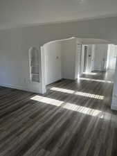 Spare room featuring arched walkways, dark wood-type flooring, and built in shelves