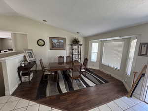 Dining area with lofted ceiling, light tile patterned floors, and a textured ceiling