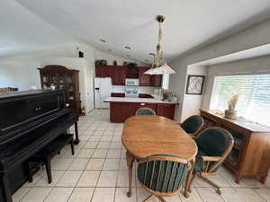 Dining space with vaulted ceiling, light tile patterned floors, and a textured ceiling