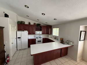 Kitchen featuring light countertops, white appliances, light tile patterned floors, vaulted ceiling, and a peninsula